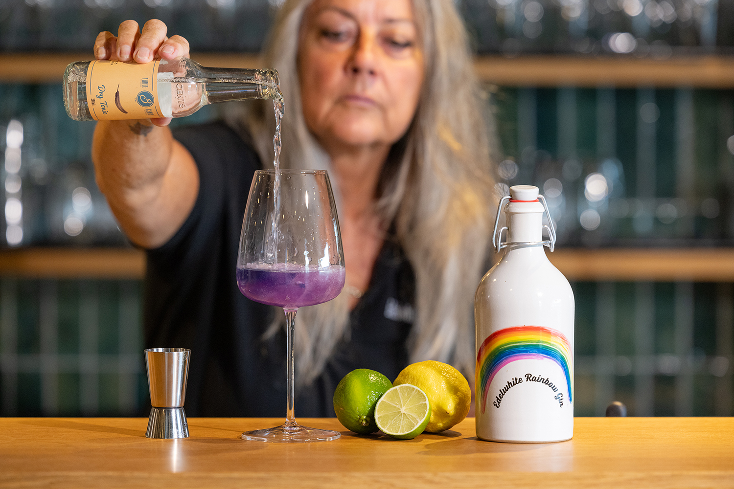 Eine Frau schenkt lila Flüssigkeit in ein Glas ein, um einen Edelwhite Rainbow Gin & Tonic zu kreieren.